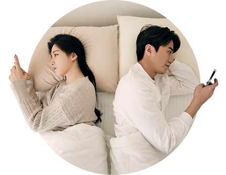 침대에서 등을 맞대고 각자 휴대전화를 보는 남녀