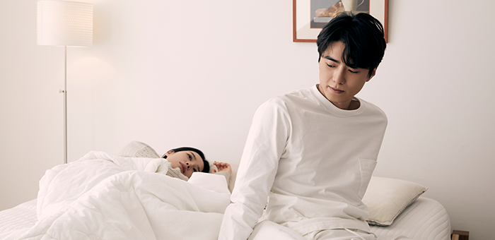누워 있는 여성 옆에서 침대에 앉아 뒤를 돌아보는 남성