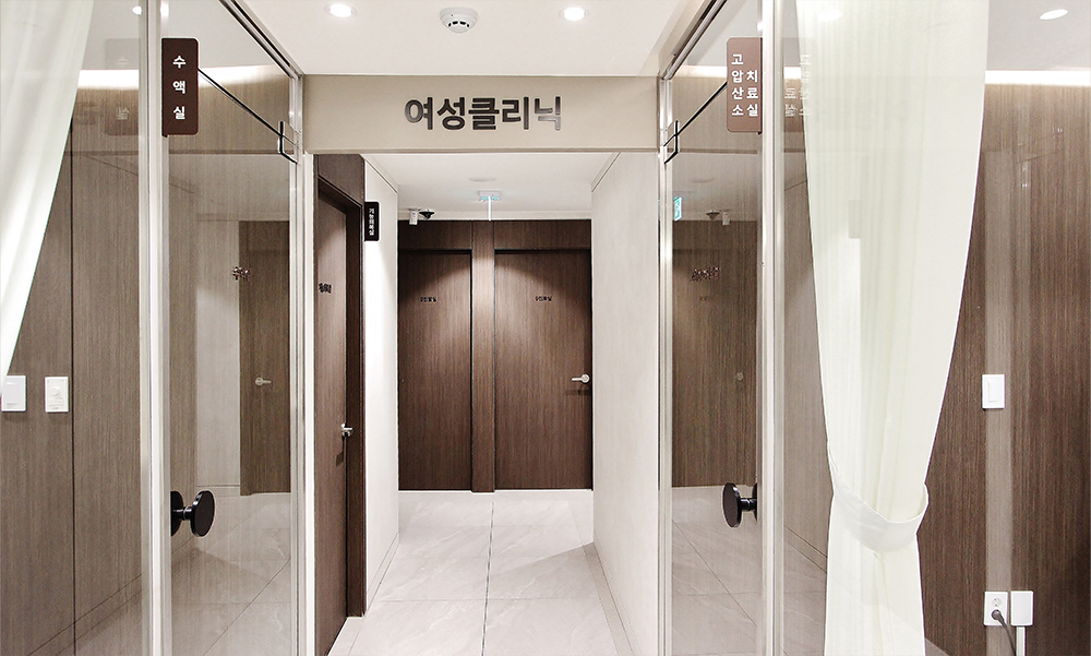 잠실 산비오의원 여성클리닉 표지 아래 유리문과 커튼을 지나 이어지는 복도