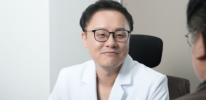 흰 가운의 의사가 마주 앉은 사람을 바라보는 모습