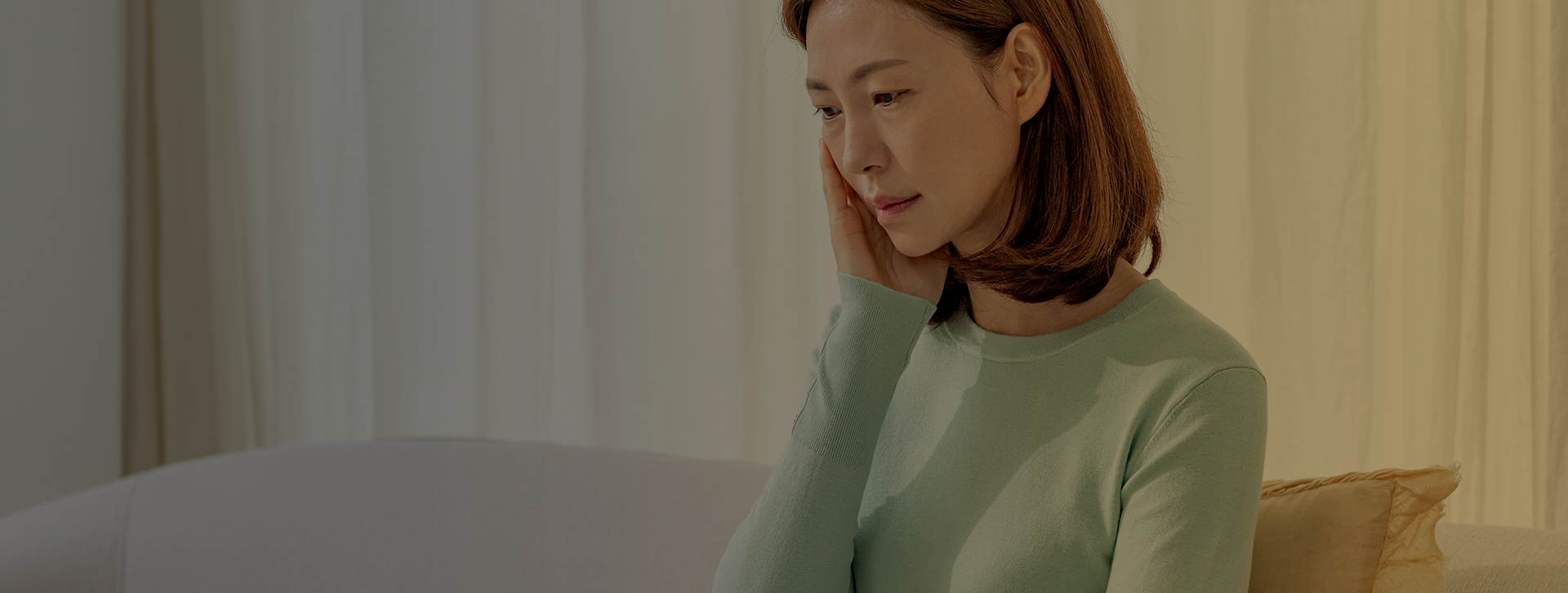 초록색 상의를 입고 소파에 앉아 아래를 바라보는 여성