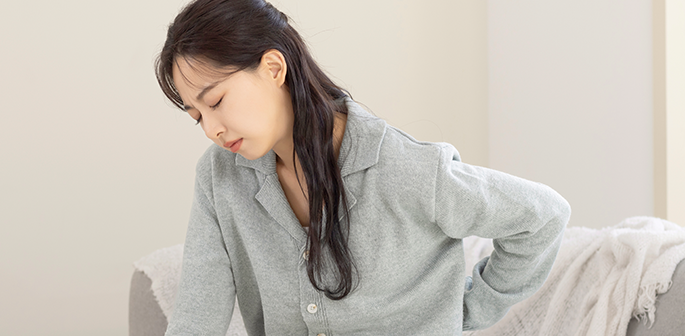 회색 잠옷을 입고 소파에서 허리에 손을 대며 고개를 숙인 여성
