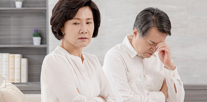 흰 옷을 입고 소파에 앉은 여성과 이마를 짚은 남성