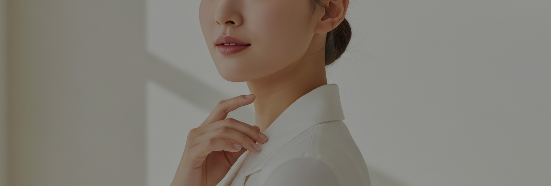 흰 블라우스를 입고 턱 가까이에 손을 댄 여성의 상반신