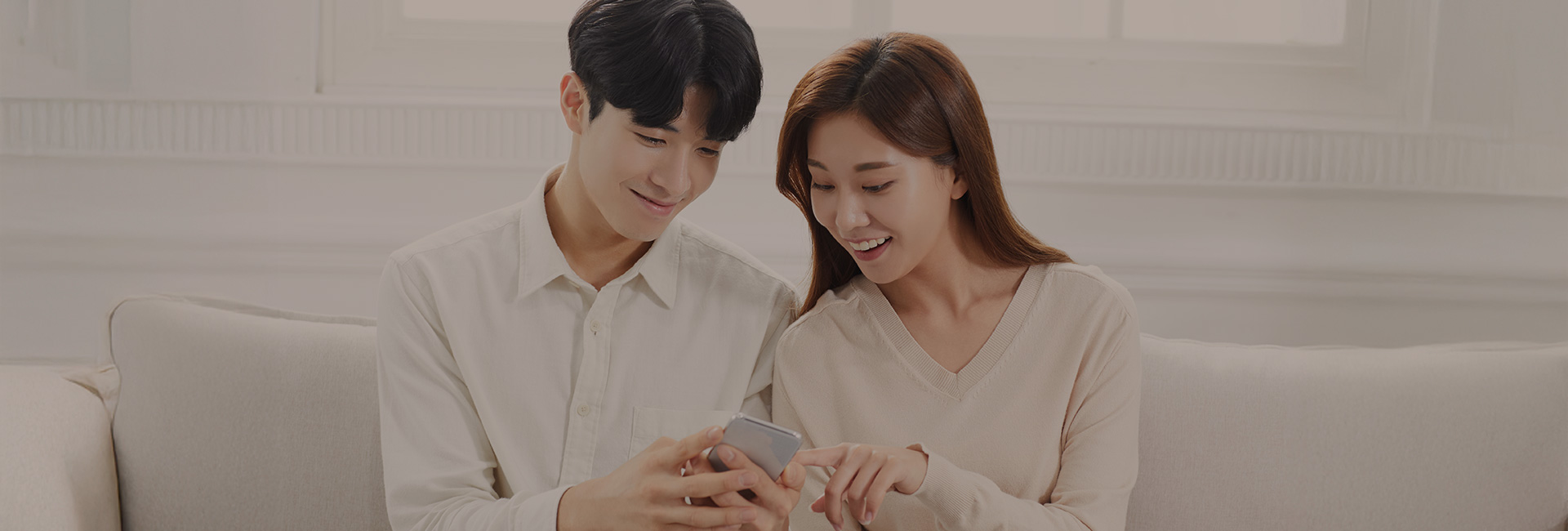 소파에 나란히 앉아 손 쪽을 내려다보는 남녀