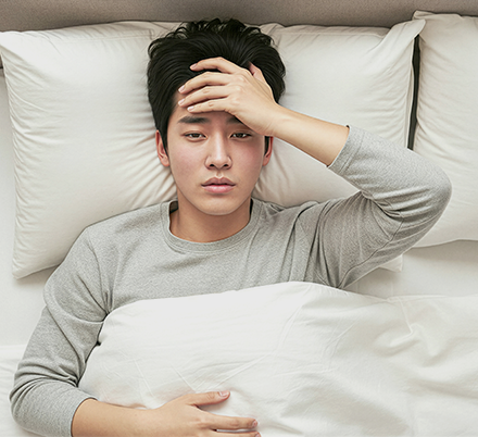 침대에 누워 한 손을 이마에 댄 남성
